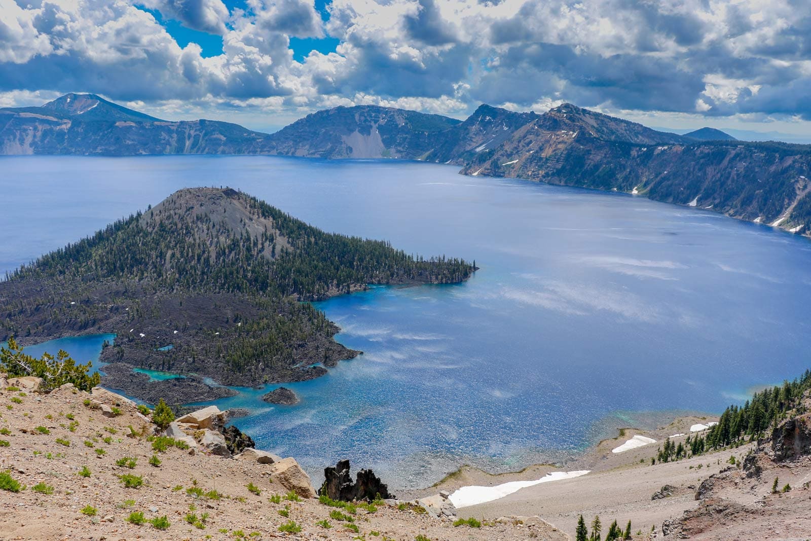 The deep, impossibly blue water of Crater Lake with Wizard Island in the center, one of the top US national parks.