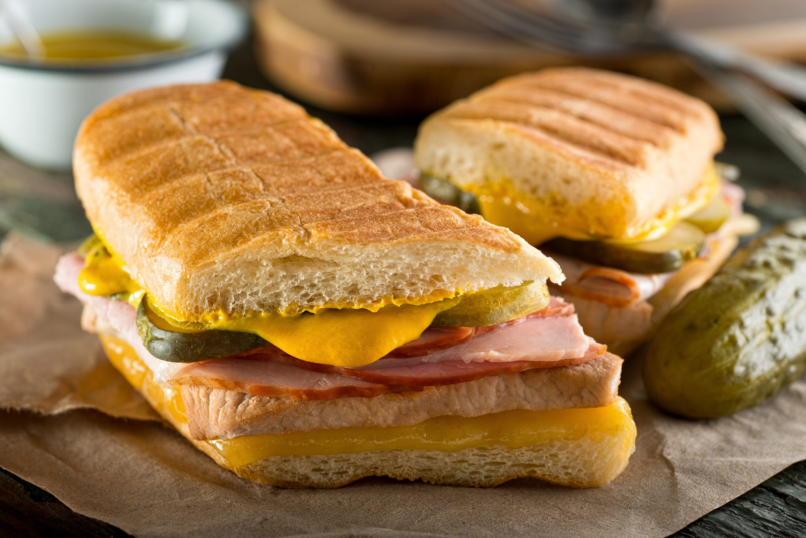 A classic Sandwich Cubano pressed until golden, showing layers of roast pork, ham, melted Swiss cheese, and pickles.