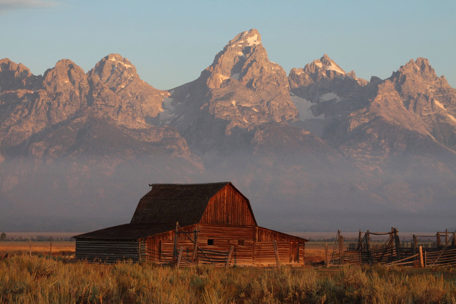 The famous Moulton Barn on Mormon Row with the jagged Teton Range in the background at sunrise.