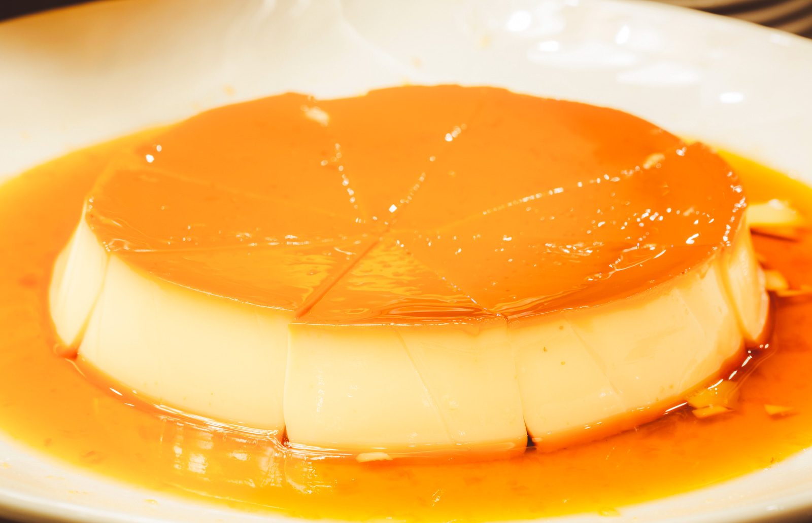 A perfect Cuban flan on a small plate, with a rich, dark caramel sauce dripping down the sides of the custard.