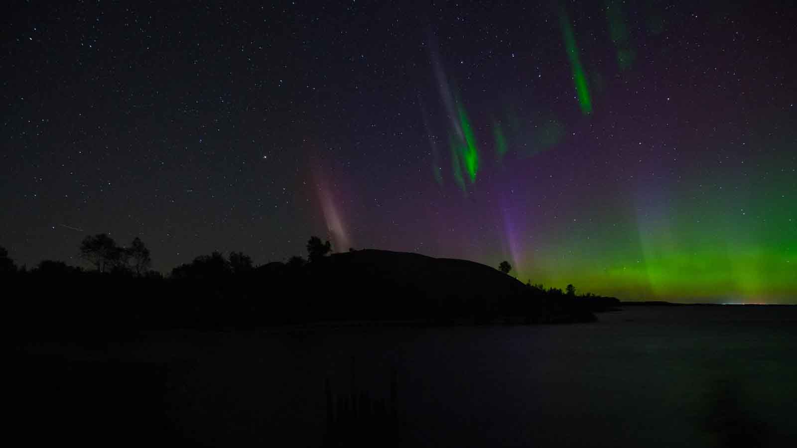 A vibrant aurora borealis, or Northern Lights, dancing in the dark sky over Lake Superior on the remote Keweenaw Peninsula
