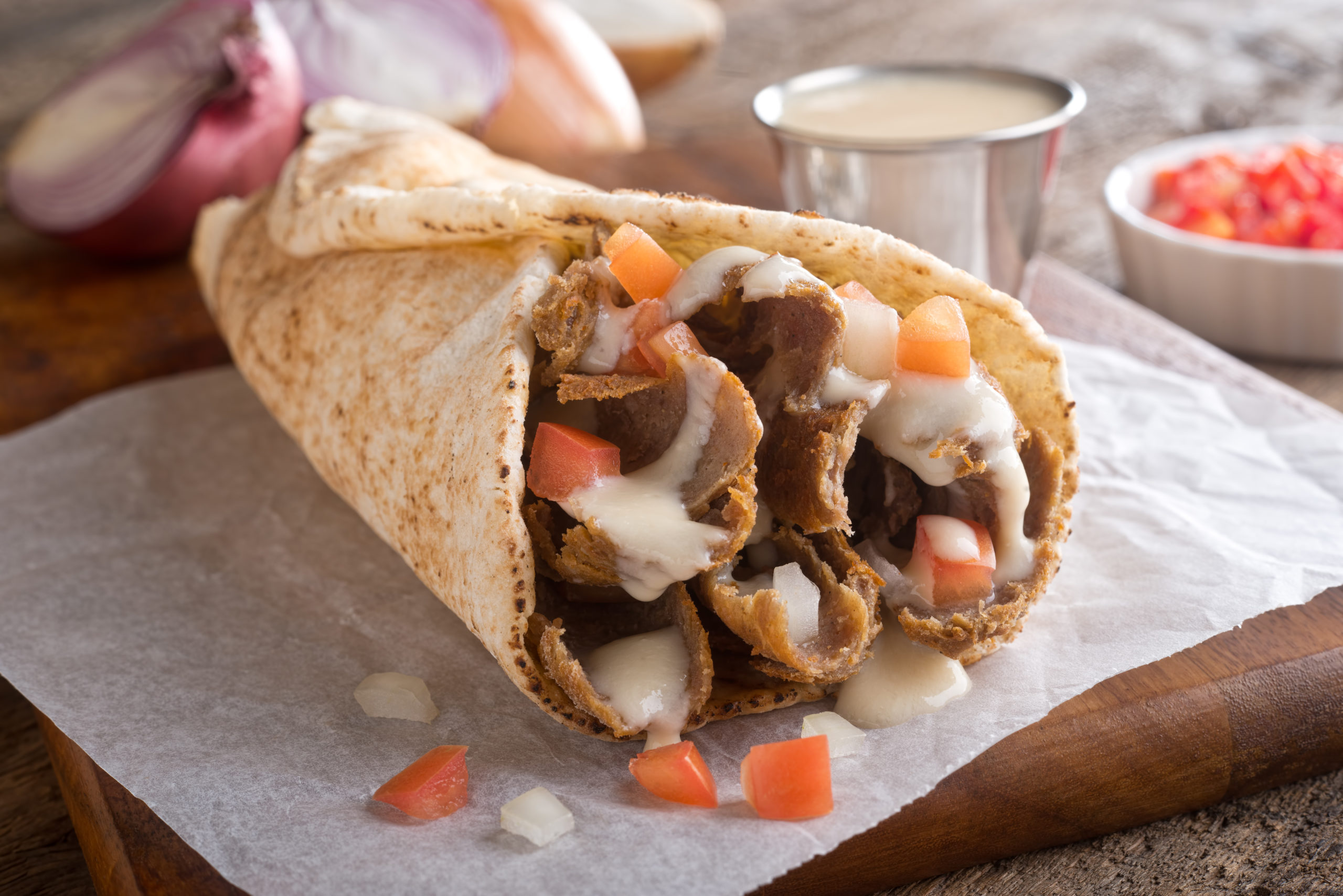 A close-up of a Halifax donair wrapped in foil, showing the meat and sweet donair sauce.