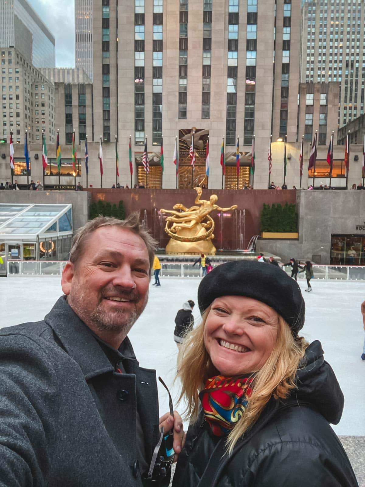 Dave and Deb from The Planet D smiling in front of Rockefeller Center at Christmas in New York City.