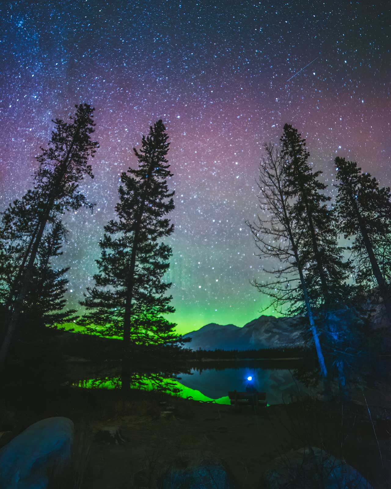 The brilliant Milky Way galaxy visible in the dark night sky with northern lights over the mountains in Jasper, a designated Dark Sky Preserve.
