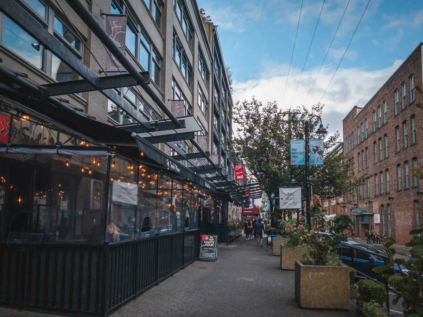 The trendy brick and beam architecture of Yaletown, with people dining on outdoor patios along Mainland Street.